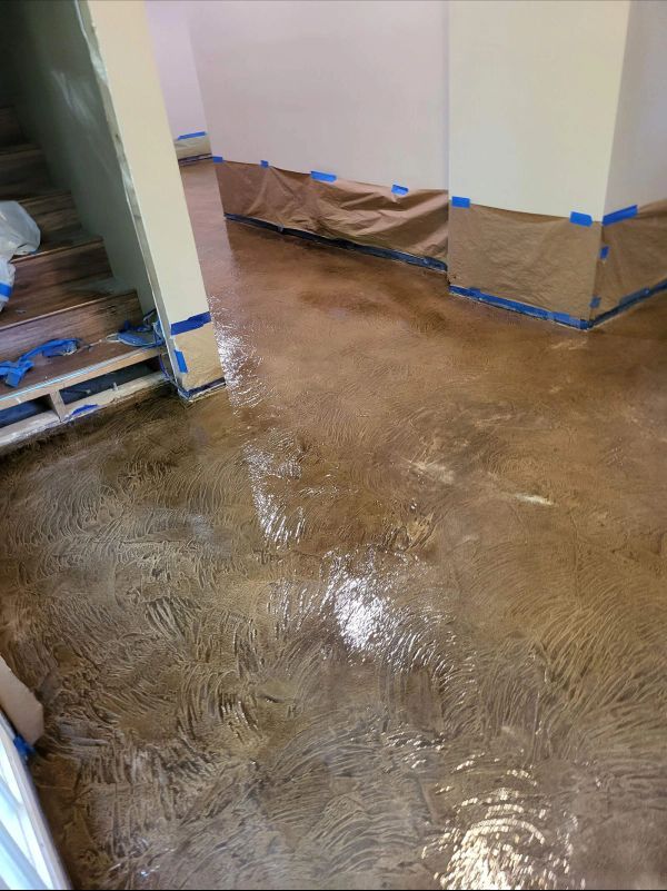 Brown stained concrete floor with water, taped walls, and unfinished stairs.