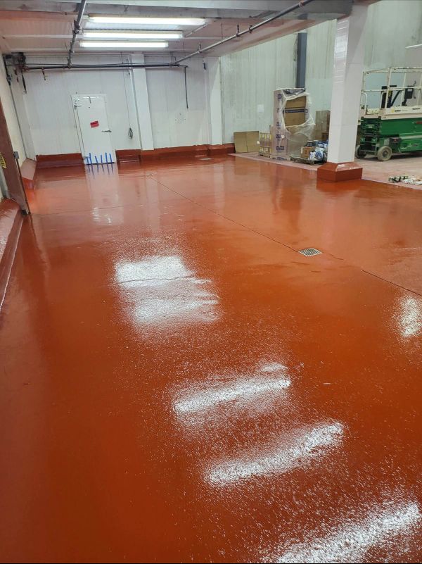 Red industrial floor with white scattered substance; interior of a room with a door and fluorescent lights.