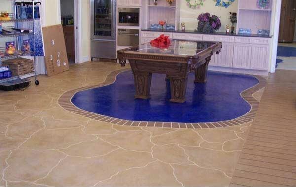 Interior with a pool-shaped blue floor around a pool table, surrounded by stone-like beige flooring and a brick border.