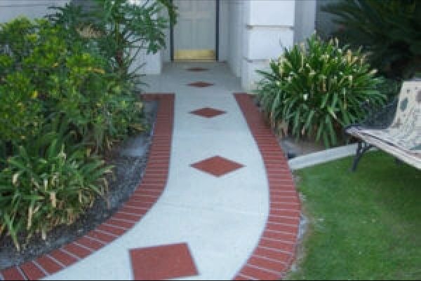 Pathway with red brick border and diamond inlays, flanked by bushes and grass.