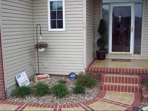Tan house exterior with flower bed, stone border, brick steps, and a front door.