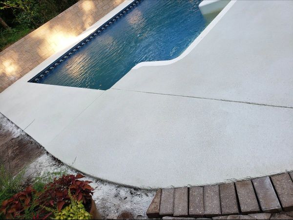 Concrete pool deck with water, brick edging, and landscaping.