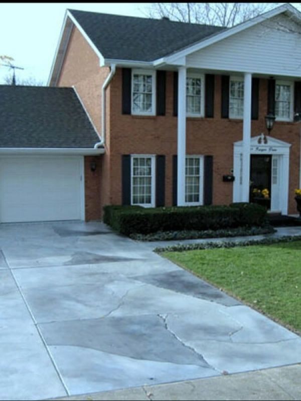 Brick house with a large white column, a gray driveway, and a garage.