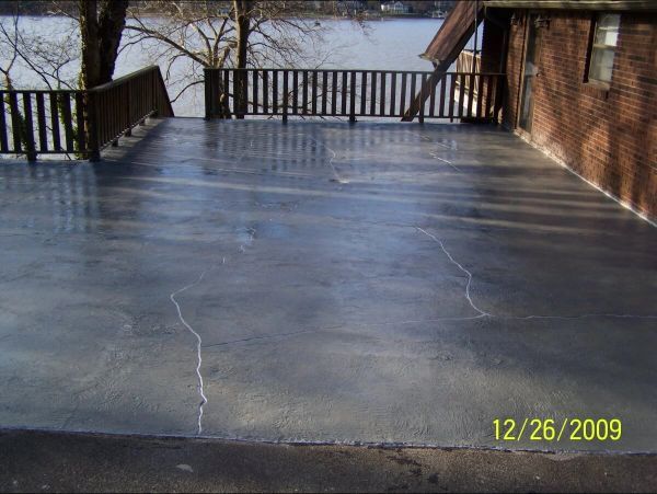 A gray concrete deck with cracks, overlooking water. Wooden railings on the left. Brick building on right.