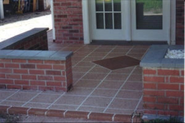 Brick porch with red-brown tiles. Brick walls with dark blue cap stones flank the entrance.