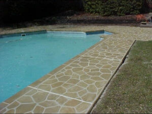 Poolside concrete paving with a stone-like pattern, bordered by pool water and lawn.