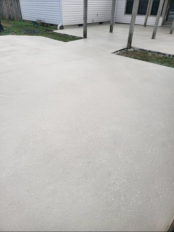 Light gray concrete patio with wooden posts, grass accents, and a white building.