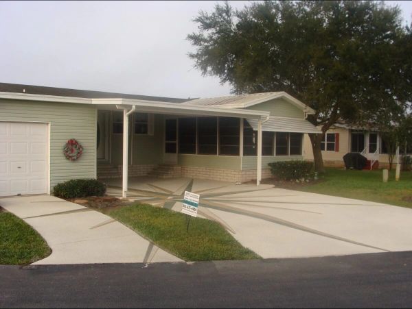 Light green single-story home with a screened porch and driveway with a decorative sunburst design.