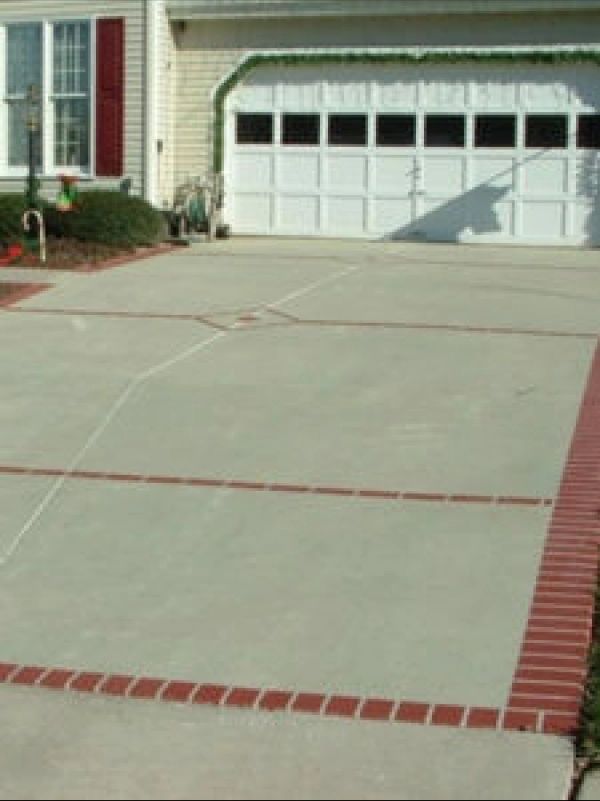 Concrete driveway with red brick border, leading to a white garage door.