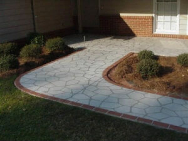 Stone walkway with brick border, leading to a house entrance, bordered by bushes and mulch.