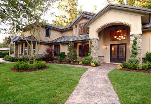 Upscale two-story house with a lush green lawn and a stone path leading to the arched entryway.