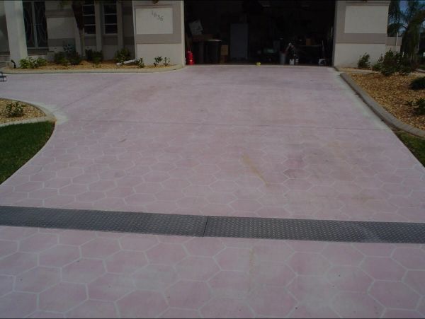 Pink concrete driveway leading to a garage, with a grey drainage strip and landscaping on the sides.