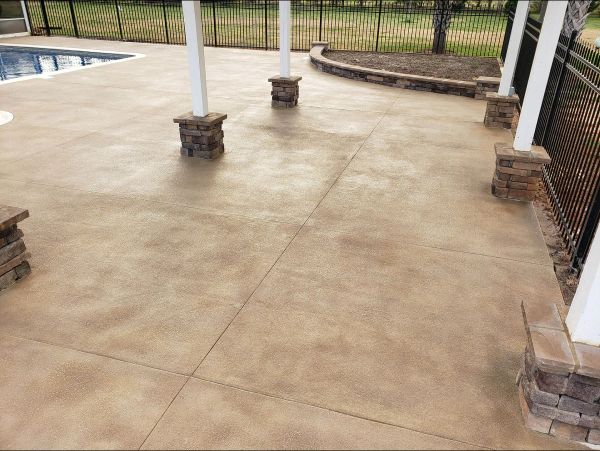 Concrete patio with stained finish, pool, pillars, and surrounding fence.