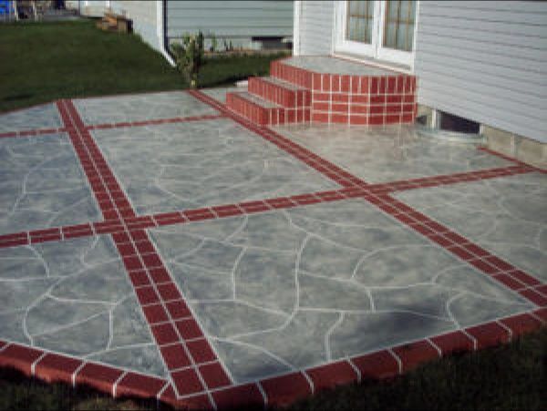 Concrete patio with red brick borders and accents next to a light gray house.