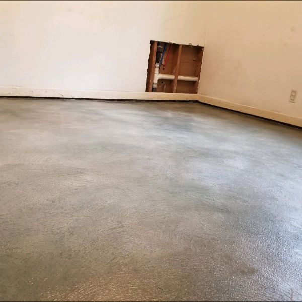 Empty room with gray concrete floor, white walls, and a hole in the wall showing exposed wood.
