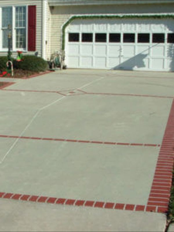 Concrete driveway with red brick borders and accents in front of a house with a white garage door.