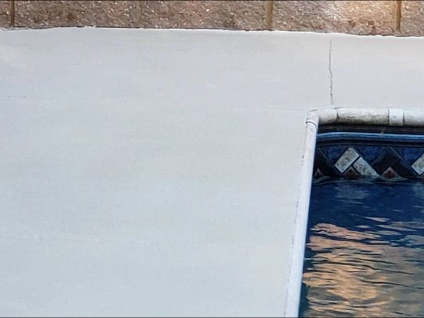 Pool edge with light-colored concrete deck, next to textured brown wall and tiled pool border.