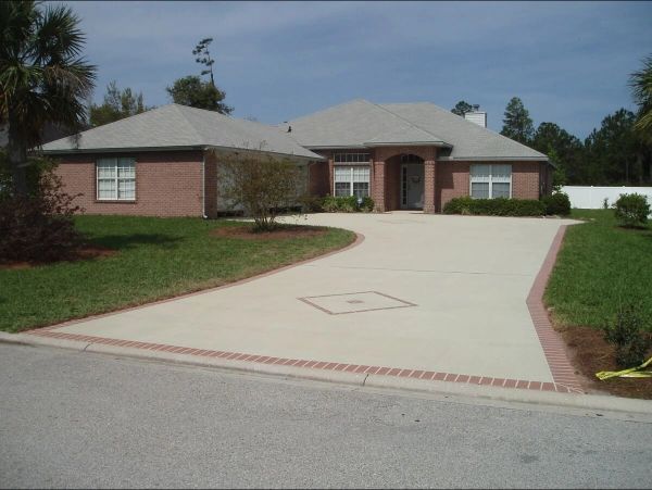 Brick house with driveway outlined in brick, surrounded by grass and trees.