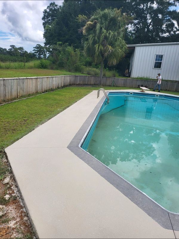 Backyard pool with concrete surround, green lawn, and fence; person near diving board.