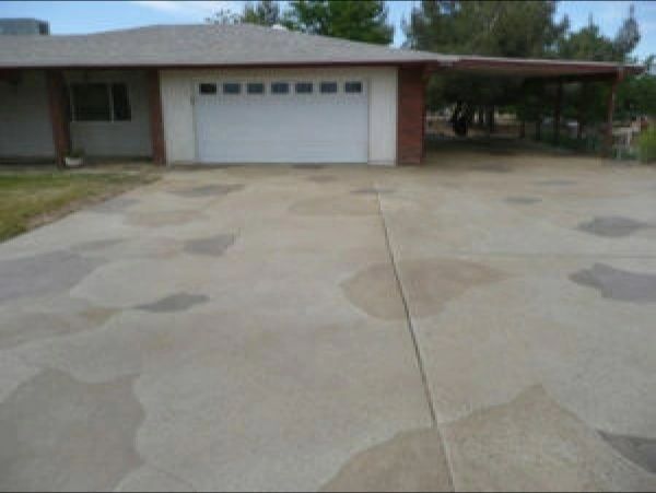 A driveway leading to a house with a white garage door and carport; the concrete has faded patches.