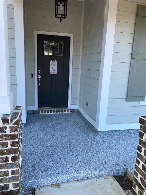 Front porch with gray speckled concrete flooring, dark door, and light green siding.