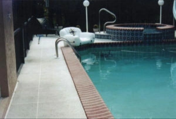 Poolside scene with pool, hot tub, and deck. The water is blue.