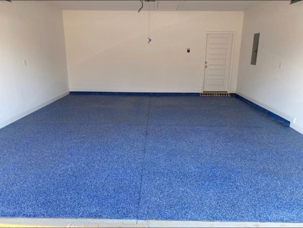 Blue speckled epoxy floor in a white-walled garage, with a door in the back and an open doorway in front.