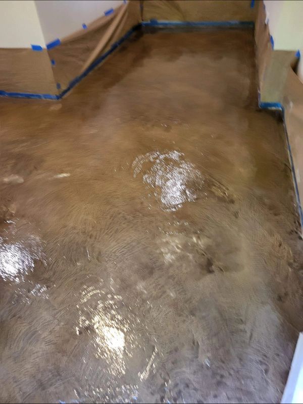 Metallic brown flooring with areas of lighter color and puddles, partially taped walls in the background.