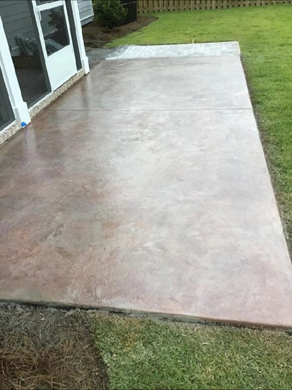 Brown stained concrete patio next to a house and grass lawn.