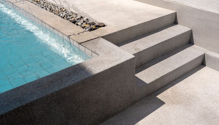 Steps leading into a pool with turquoise water; textured gray concrete.