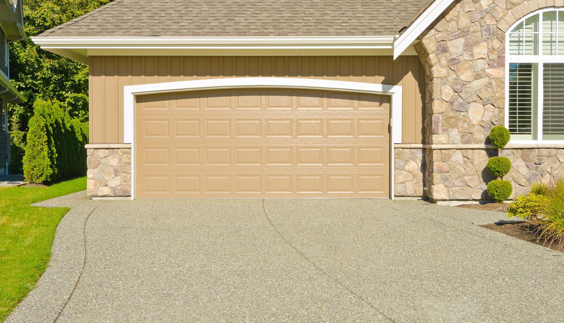 Tan garage door on a house with stone accents, beige siding, and a gravel driveway.