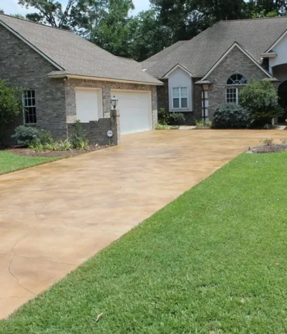 Driveway leading to a brick house with attached garage, green lawn.