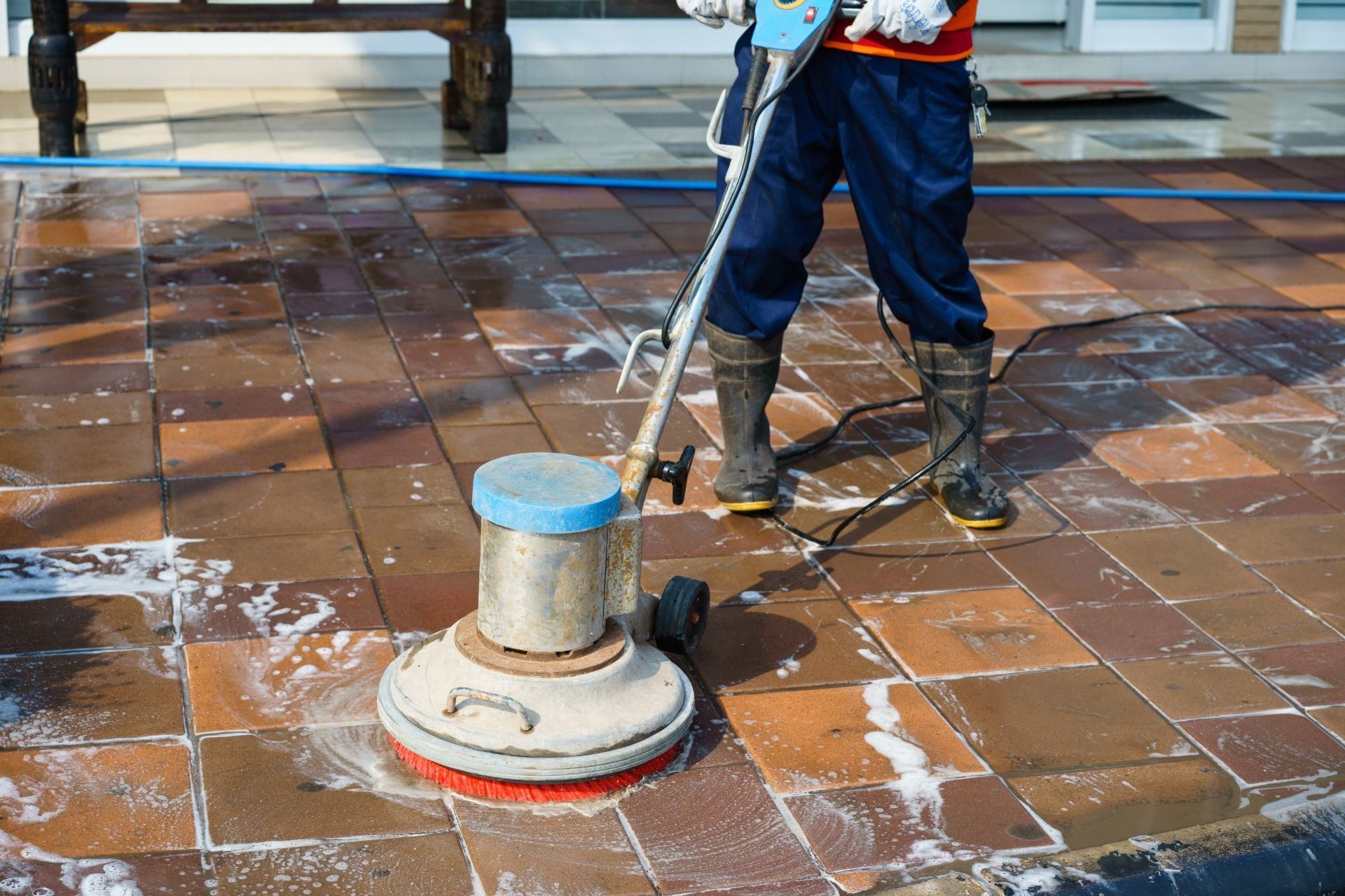 Persona che pulisce un patio in mattoni con una lavasciuga pavimenti; all'aperto.