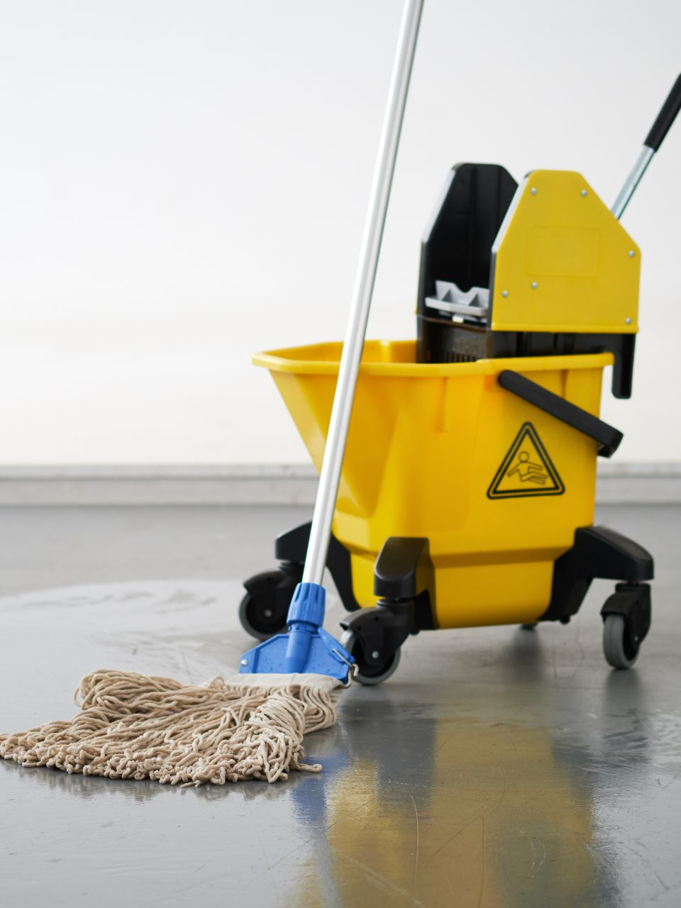 Secchio giallo con strizzatore e mocio su pavimento grigio e bagnato.