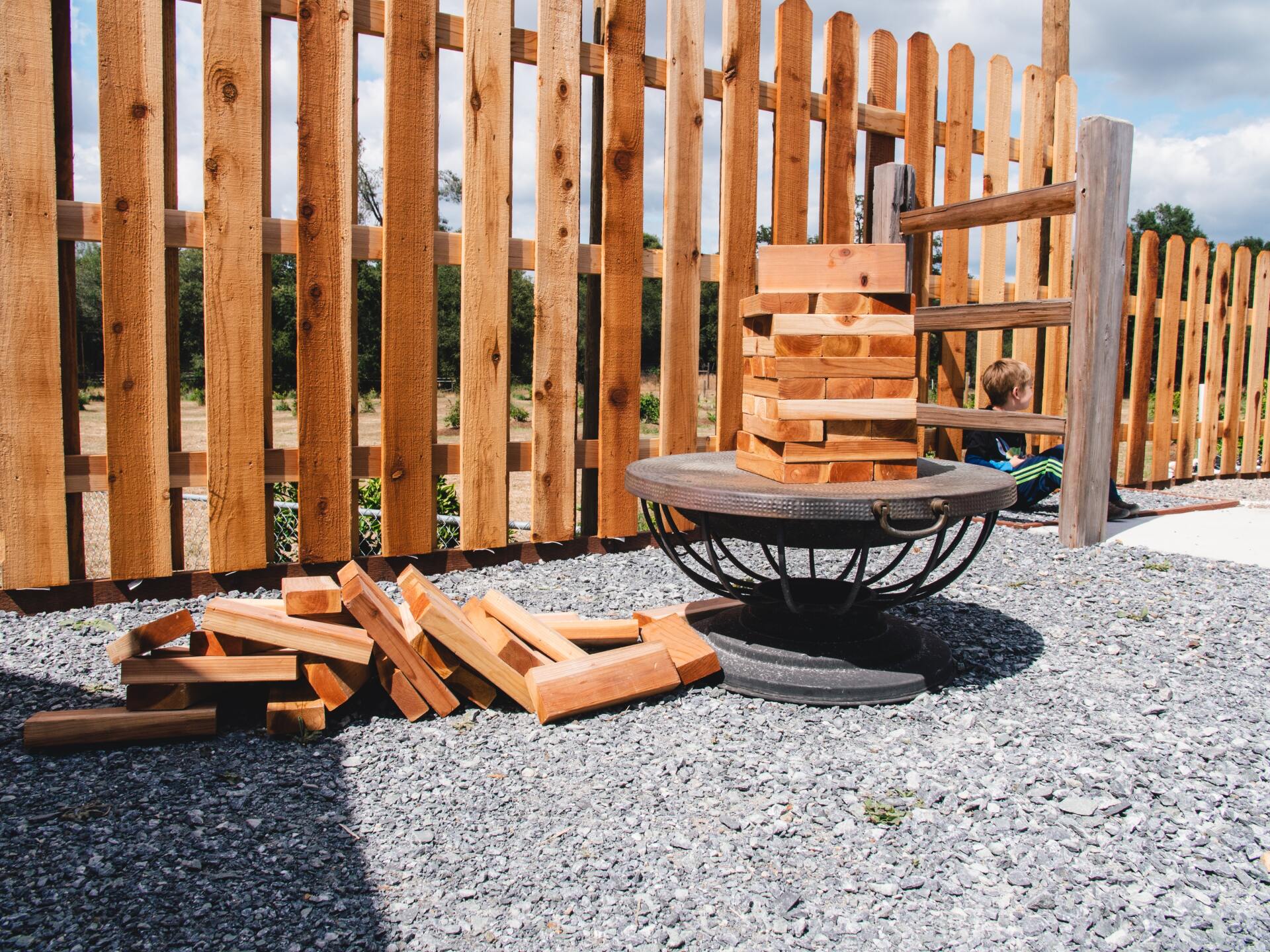 Wooden block game on a tire-based table, with scattered blocks, by a wooden fence.