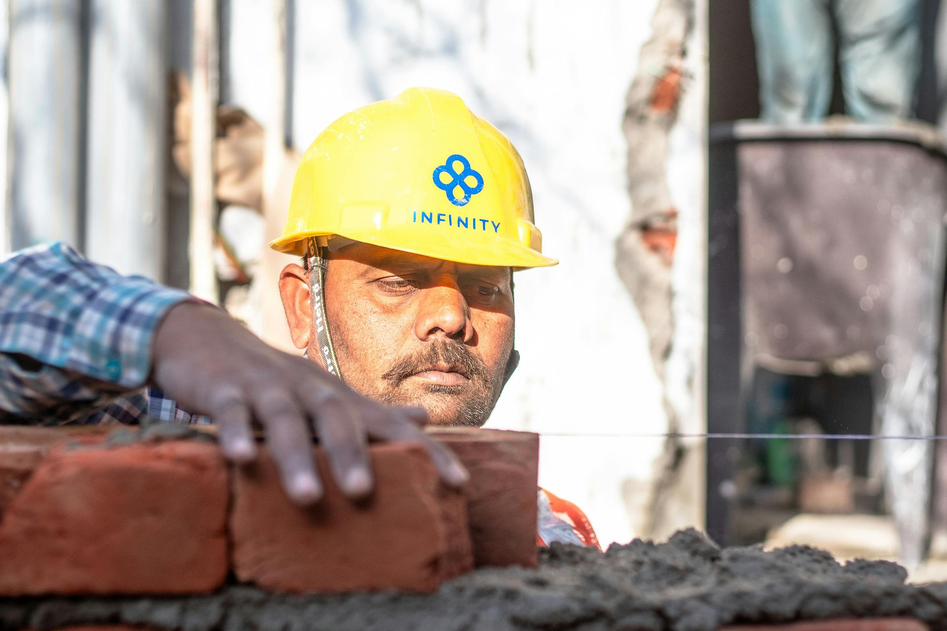 Construction worker in yellow hard hat laying bricks.