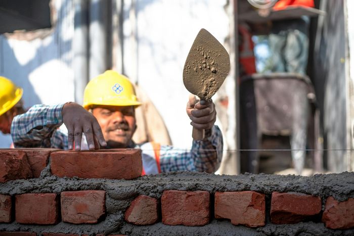 Construction worker in yellow hard hat, using trowel to lay bricks.