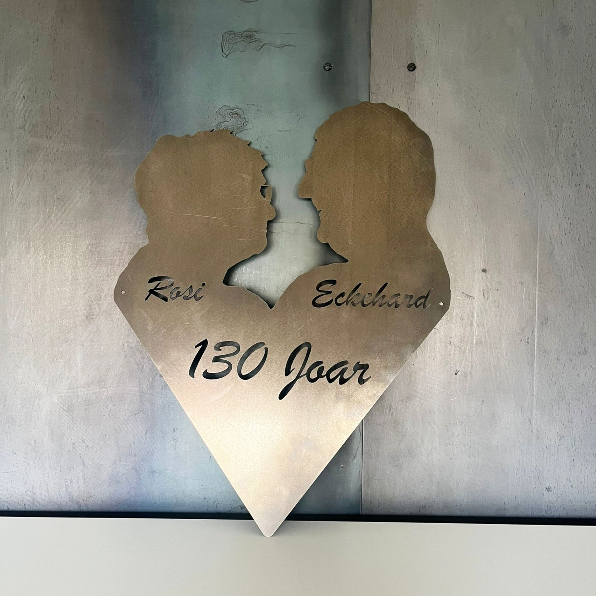Metallherz mit den Silhouetten eines Paares, den Namen „Rosi“ und „Eckhard“ sowie dem Schriftzug „130 jaar“ 