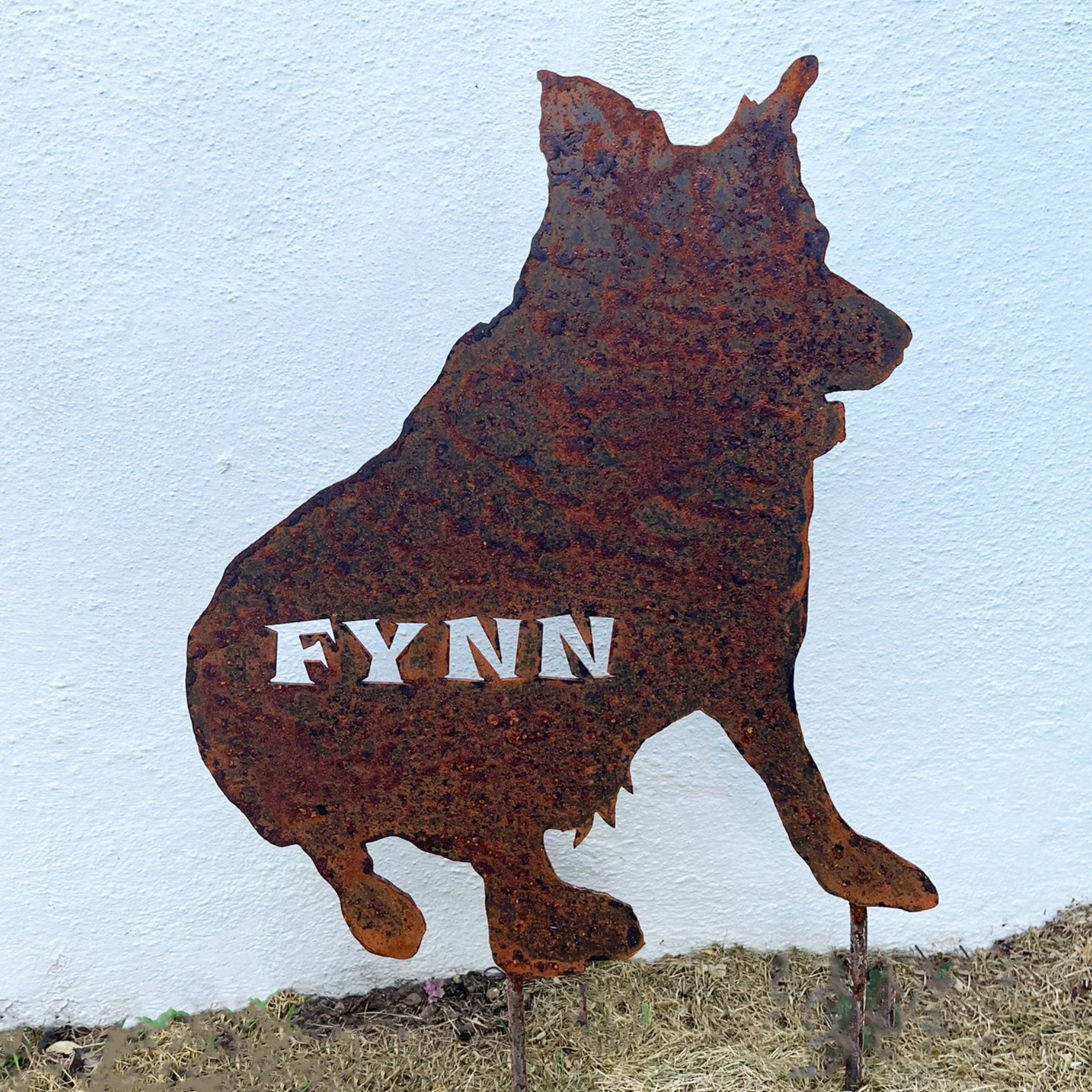 Die rostige Metallsilhouette eines Hundes namens Fynn, sitzend, auf einem Metallpfahl.