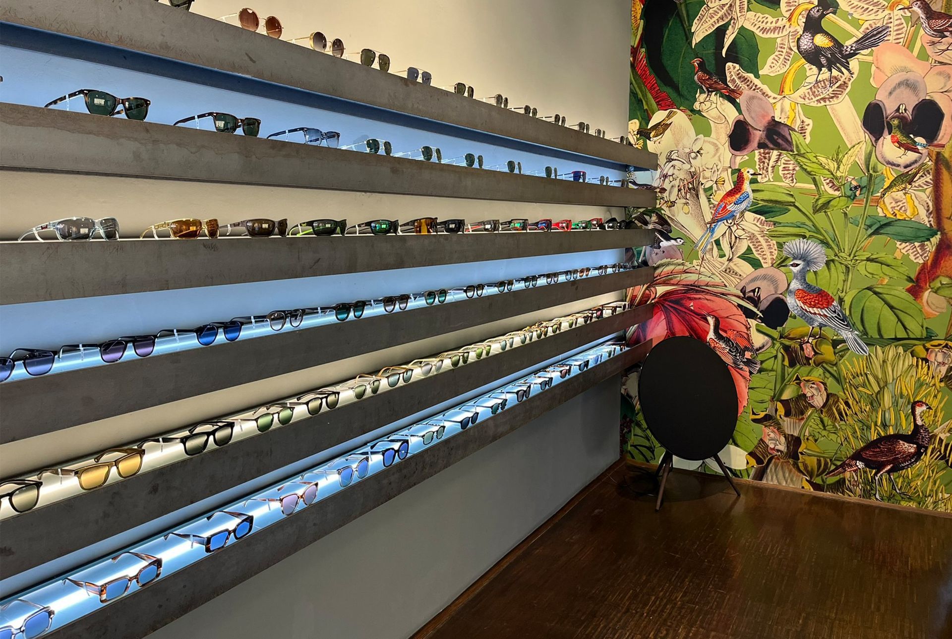 Sonnenbrillen werden in einem Geschäft auf mehreren Regalen, im Hintergrund ist ein farbenfrohes Wandgemälde zu sehen.
