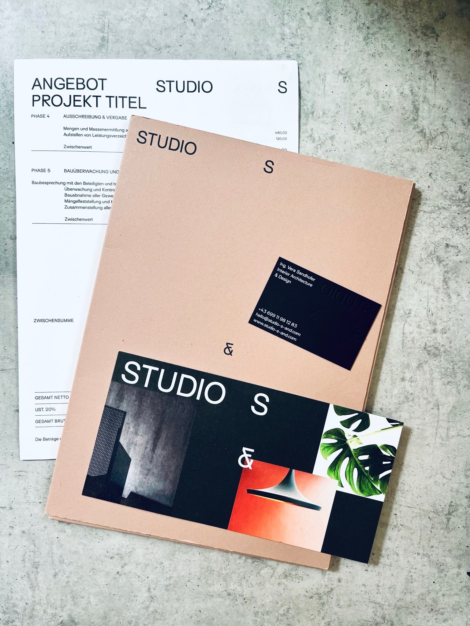 Rosa Mappe und weißes Papier mit dem Aufdruck „STUDIO“, verschiedene Gestaltungselemente auf grauem Untergrund.