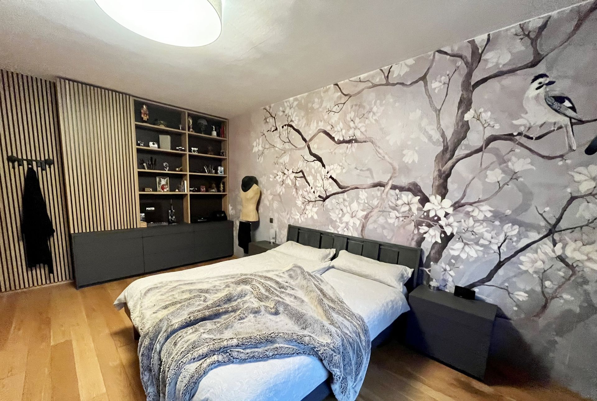 Schlafzimmer mit Holzboden, Akzentwand mit einem Baummotiv, Bett und Person.