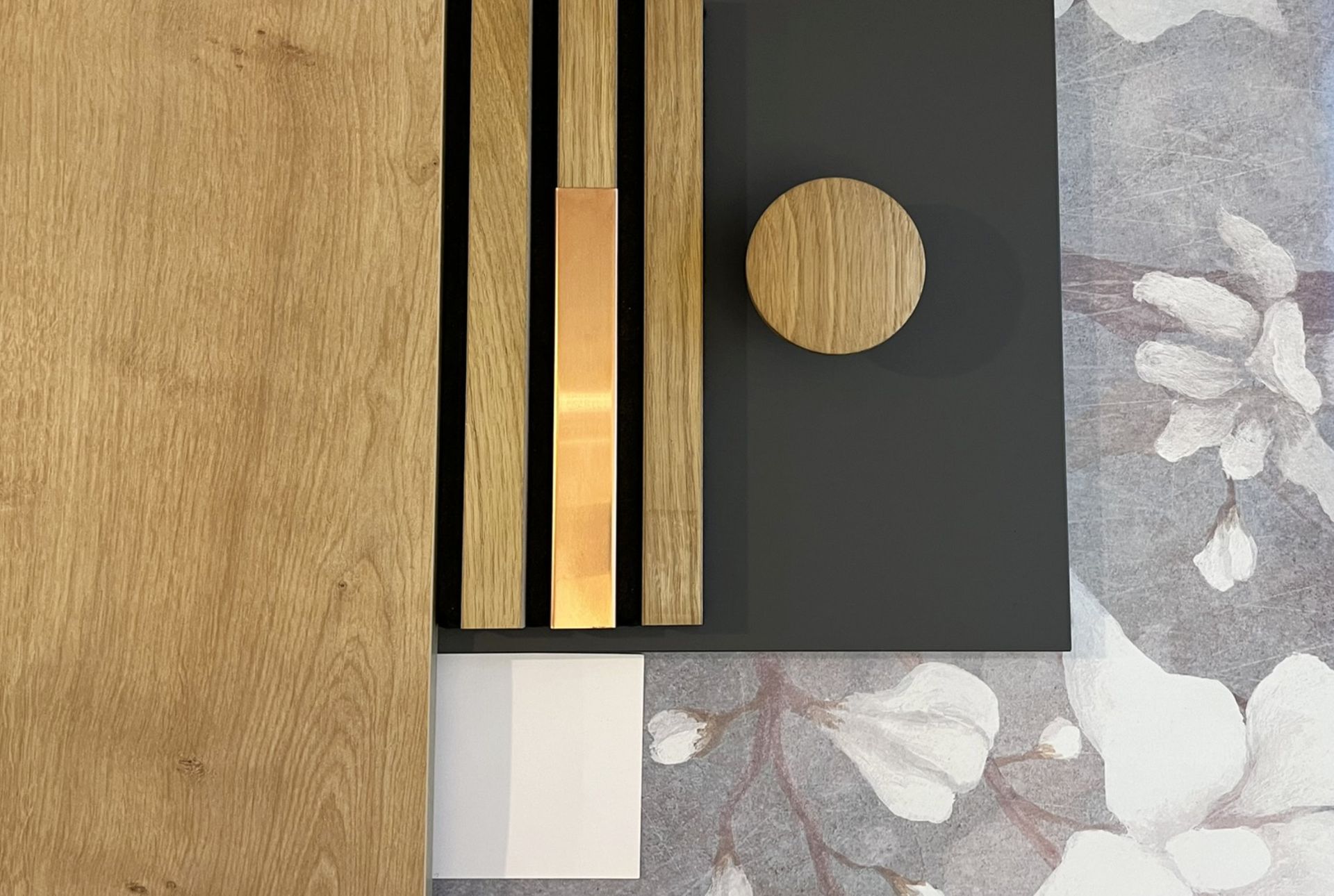 Moodboard: Holzmaserung, schwarze Lamellen mit Kupfer, Dunkelgrau, florale Tapete und runder Holzknopf.