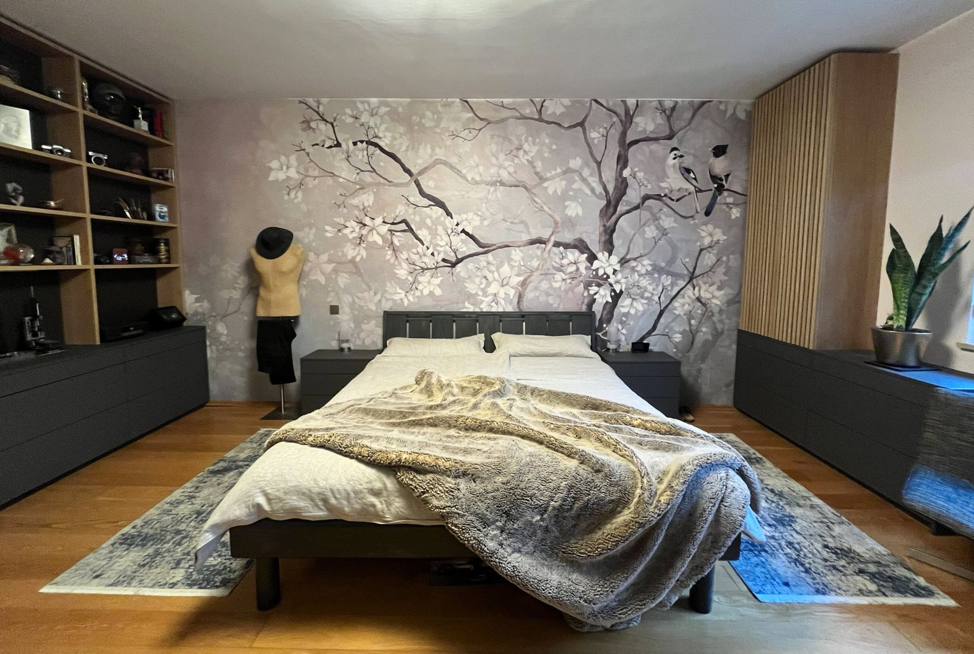 Schlafzimmer mit Bett, Baum-Wandbild, Einbauschränken und Holzboden.