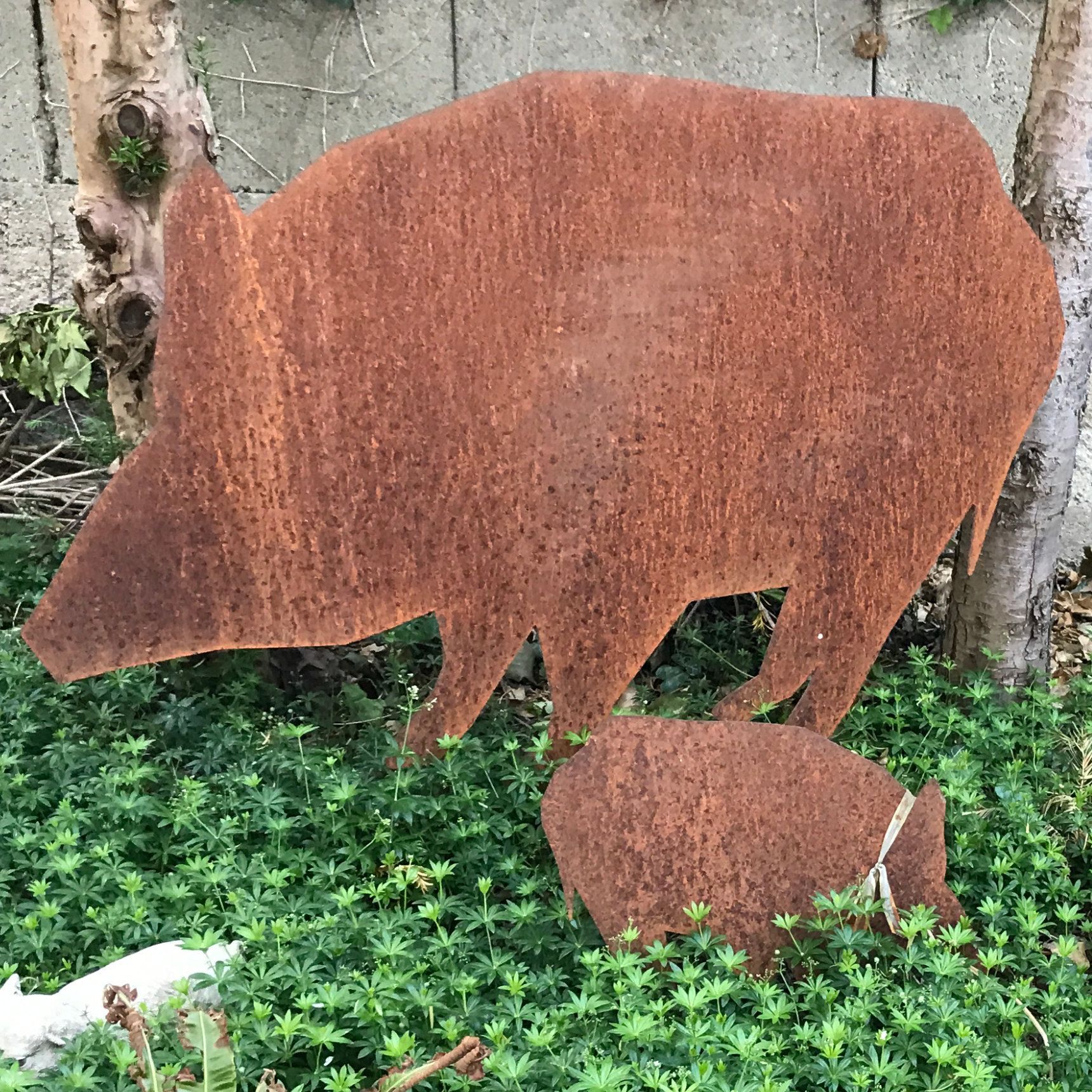 Rostige Metallskulptur eines Wildschweins und eines kleineren Ferkels in einer Gartenlandschaft.