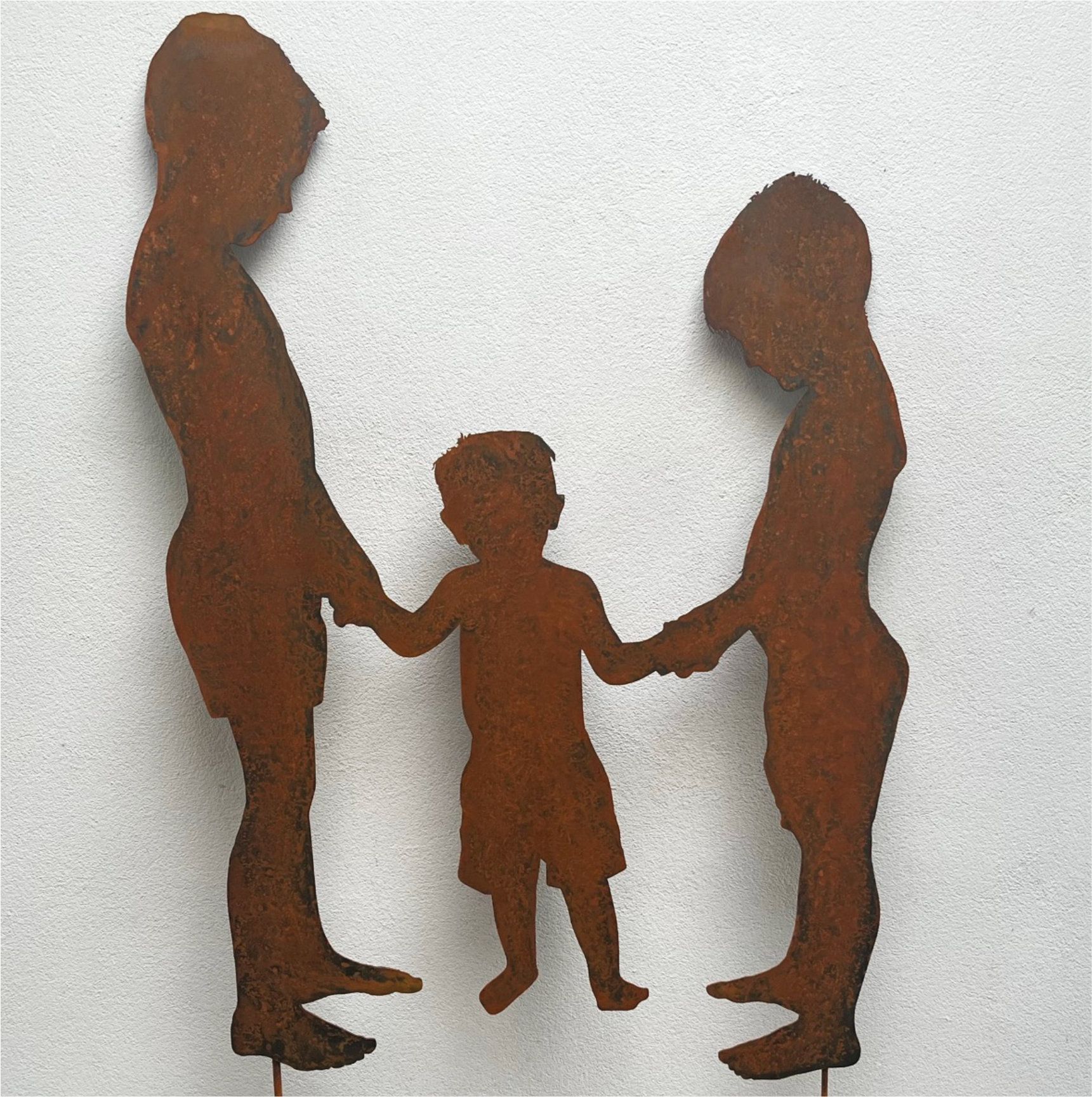 Metallskulptur von drei Händchen haltenden Figuren, die Kinder zu sein scheinen. Rostfarben auf weißem Grund.