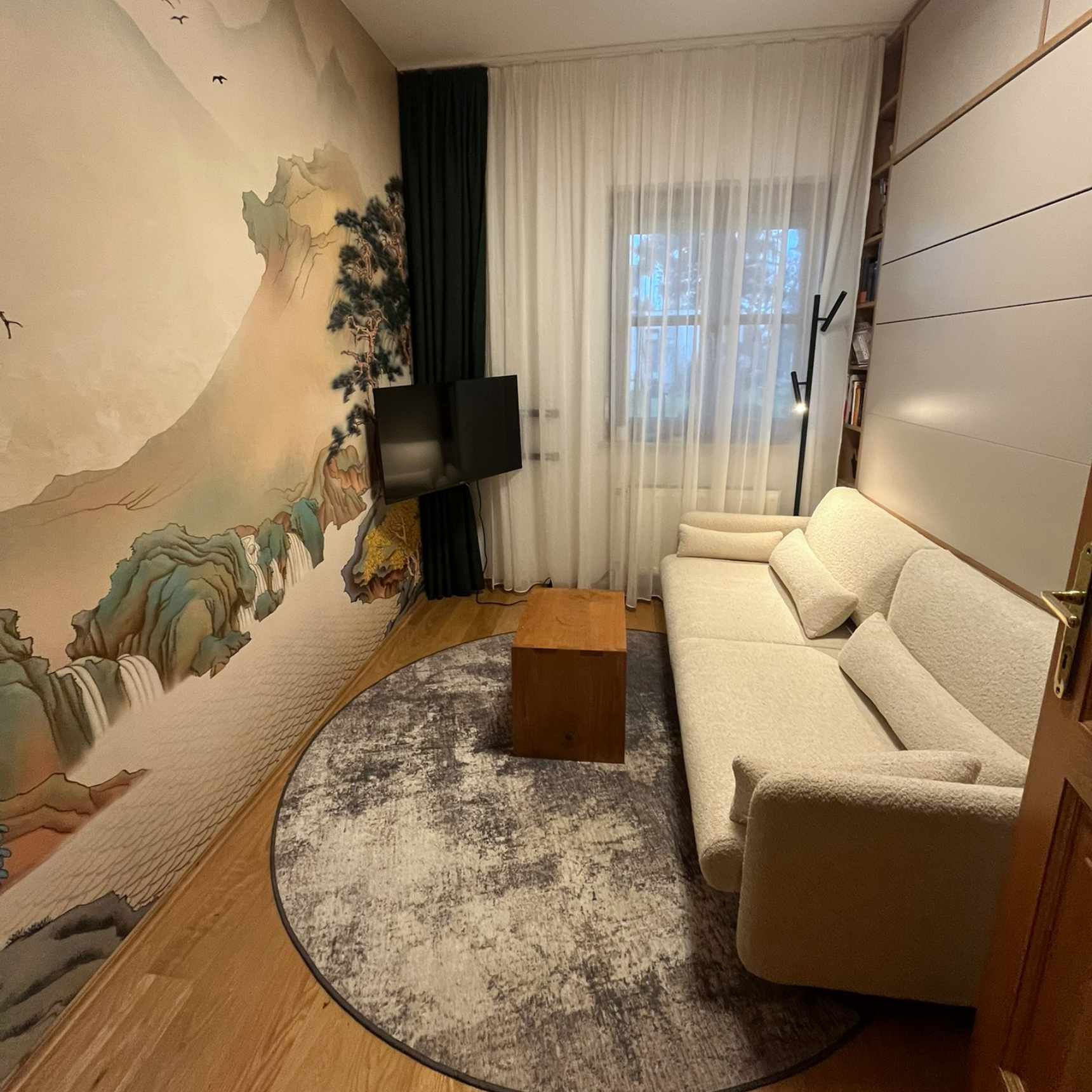 Gemütliches Wohnzimmer mit Landschaftsgemälde, weißem Sofa, rundem Teppich und einem kleinen Holztisch.