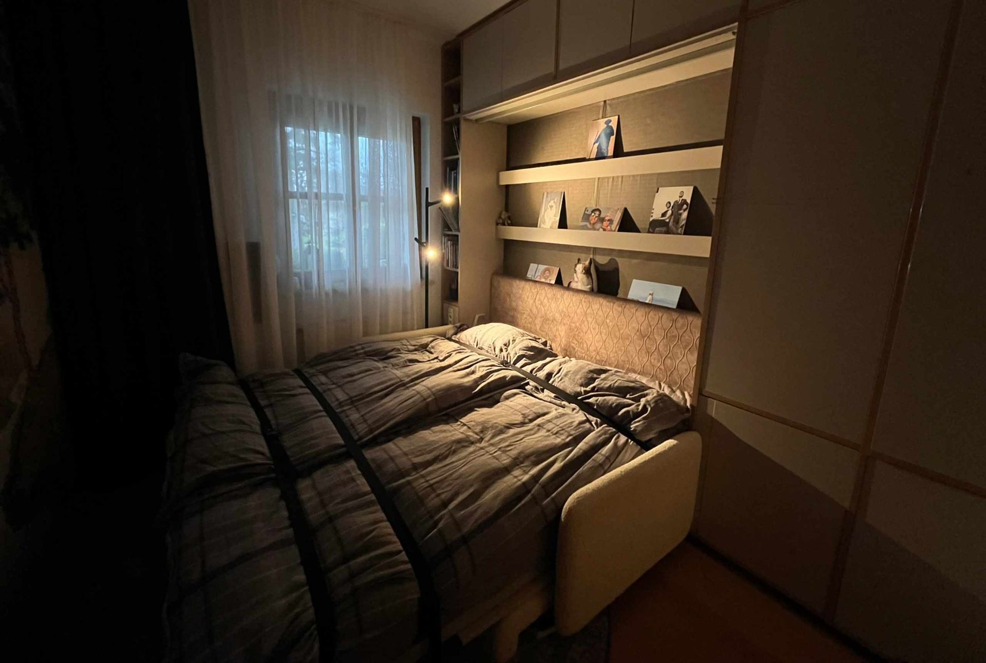Gemütliches Schlafzimmer mit Bett an einer eingebauten Wand mit Regalen und sanfter Beleuchtung.