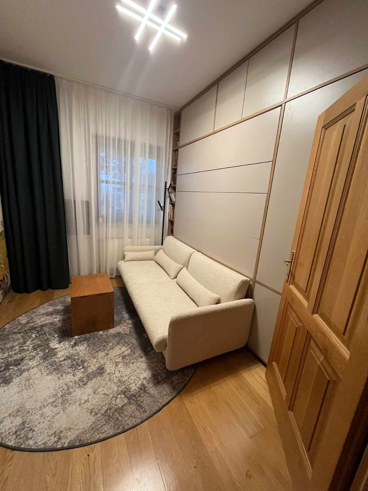 Beiges Sofa in einem Zimmer mit hellem Holzboden, einem gemusterten Teppich und einer hellen Akzentwand.