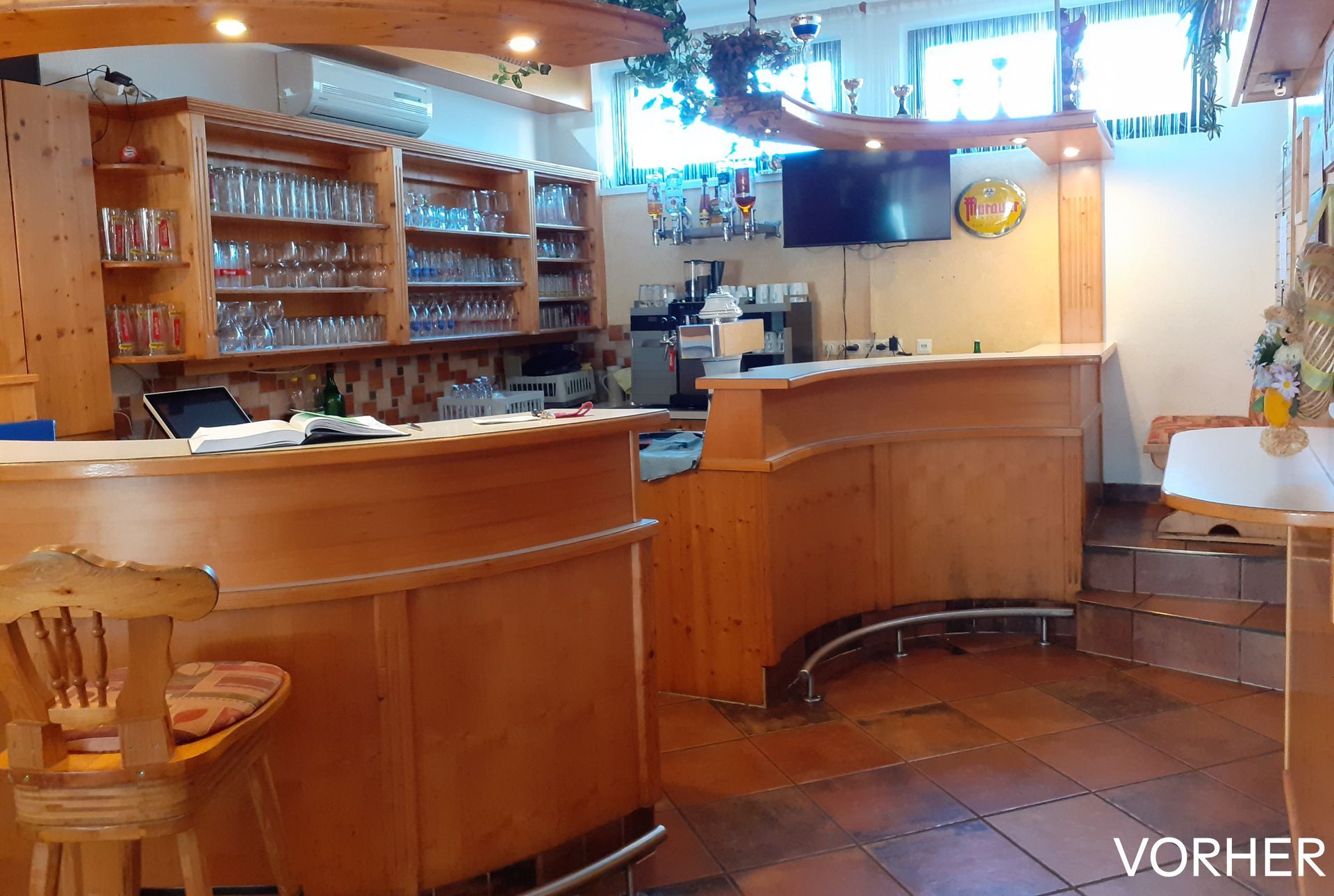 Innenansicht einer Holzbar mit Regalen voller Gläser, einem Fernseher und einigen kleinen Tischen.